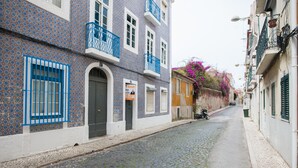 A cobblestone street lined with buildings featuring blue and white patterned facades, balconies, and a motorcycle parked on the side. - FLH Janelas Verdes Charming Flat (Lisbon)