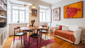 A spacious living room with a dining area, large windows, and artwork on the walls. - FLH Janelas Verdes Charming Flat (Lisbon)