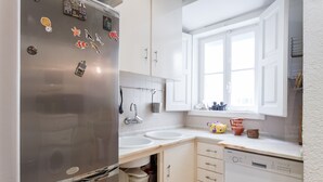 A compact kitchen with a stainless steel refrigerator, two white sinks, and a window above the sink. - FLH Janelas Verdes Charming Flat (Lisbon)
