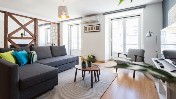 A living room with a sofa, a round coffee table, a desk with a lamp, and large windows.