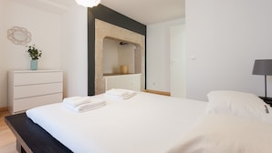 A modern hotel room with a bed, a bedside table, a lamp, a dresser, and a mirror.