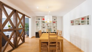 A dining area with a wooden table and chairs, a white ceiling, and shelves with various items.