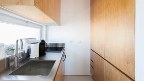 A compact kitchen with wooden cabinets, stainless steel appliances, and a window providing natural light.