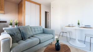 A modern living room with a grey sofa, a coffee table, and a dining area with a white table and chairs.