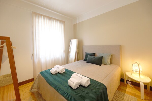 A hotel room with a bed, two towels, a bedside table with a lamp, and a window with curtains.