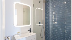 A bathroom with a white vanity, two mirrors, and a shower with blue tiles.