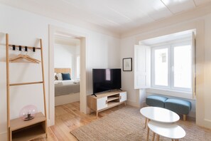 A modern living room with a TV, a sofa, a coffee table, and a wooden coat rack.