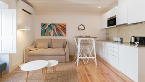 A compact living space with a kitchenette, a sofa, a small dining table, and a painting on the wall.
