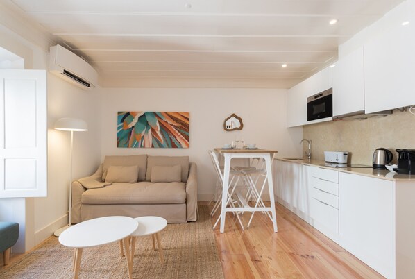 A compact living space with a kitchenette, a sofa, a small dining table, and a painting on the wall.