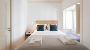 A hotel room with a bed, a nightstand, a lamp, and a window.