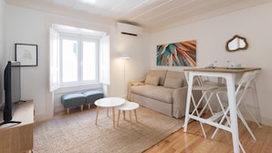A modern living room with a sofa, two round tables, a TV, and a painting on the wall.