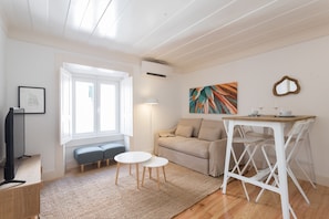 Un salon moderne avec un canapé, deux tables rondes, un téléviseur et un tableau accroché au mur.