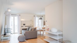Ein modernes, helles Wohnzimmer mit einer Couch, einem Hocker und einem weißen Regal.