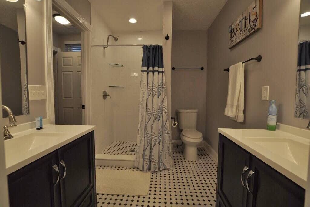 Baño con dos lavamanos, ducha e inodoro. Cuenta con un perchero y un cartel en la pared.