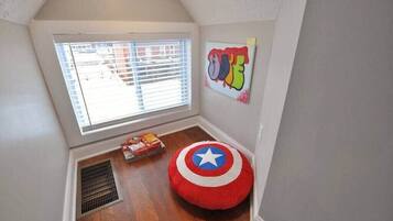 Una habitación pequeña con techo inclinado, una ventana con persianas, un radiador, un cojín redondo con diseño de estrella y una pared con un grafiti de colores.