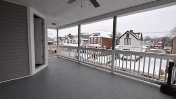 A covered porch with a white railing, a ceiling fan, and a view of neighboring houses.