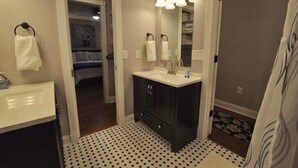 Une salle de bain avec un lavabo blanc, des meubles sombres, un miroir avec éclairage intégré et un carrelage décoratif.