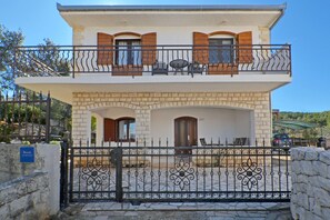 A two-story building with a balcony, a stone facade, and a gated entrance.