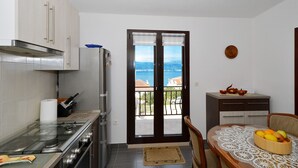 A compact kitchen with a view of the sea, a dining area with a table and chairs, and a small cabinet with a decorative plate. - LOZA 2, 4+1 Sea View apt with Garden, 80m from sea (Slatine)