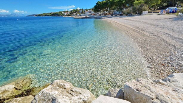 A clear beach with pebbles and rocks, a calm sea, and a row of houses in the background. - LOZA 2, 4+1 Sea View apt with Garden, 80m from sea (Slatine)