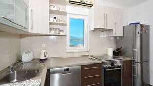 A modern kitchen with a dishwasher, oven, and refrigerator. There is a window with a view of the sea. - LOZA 2, 4+1 Sea View apt with Garden, 80m from sea (Slatine)