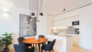 Eine moderne Küche mit weißen Schränken, einer zentralen Kochinsel und einem Essbereich mit einem runden Holztisch und Stühlen.