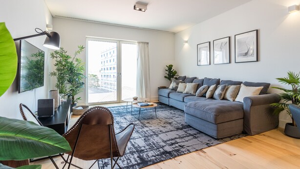 Ein modernes Wohnzimmer mit einem grauen Sofa, einem Couchtisch und einem großen Fenster mit Vorhängen.