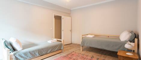 Habitación con dos camas individuales, suelo de madera, una puerta, una mesita con lámpara y una alfombra estampada.