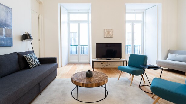 A modern living room with a grey sofa, a round coffee table, a blue armchair, and a grey sofa. - FLH Chiado Modern Apartment (Lisbon)