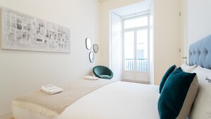 A bedroom with a bed, a chair, a window, and a door. - FLH Chiado Modern Apartment (Lisbon)