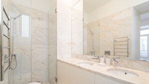 A modern bathroom with a glass-enclosed shower, two sinks, and a large mirror. - FLH Chiado Modern Apartment (Lisbon)