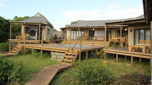 A wooden deck with a pool, a covered seating area, and a small building with a sloped roof.