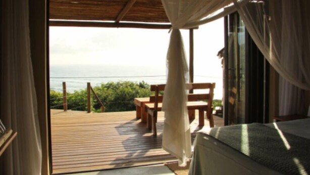 An open balcony with a wooden deck, a bed with a canopy, and a view of the ocean.
