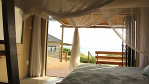 A bedroom with a bed, a wooden bench, and a view of the sea.