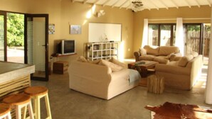 A spacious living area with a high ceiling, a sofa set, a television, and a bar area with stools.