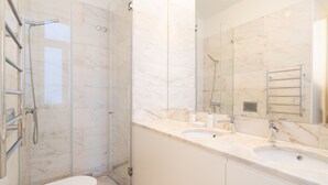Une salle de bain moderne avec une douche à parois de verre, des toilettes blanches et un comptoir en marbre doté de deux vasques.