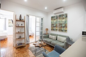 Een moderne woonkamer met een bank, een salontafel, een boekenkast en een glazen schuifdeur die leidt naar een andere kamer.