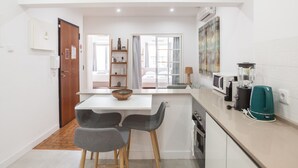 A compact kitchen with a central island, two bar stools, a microwave, a blender, and a kettle on the counter.
