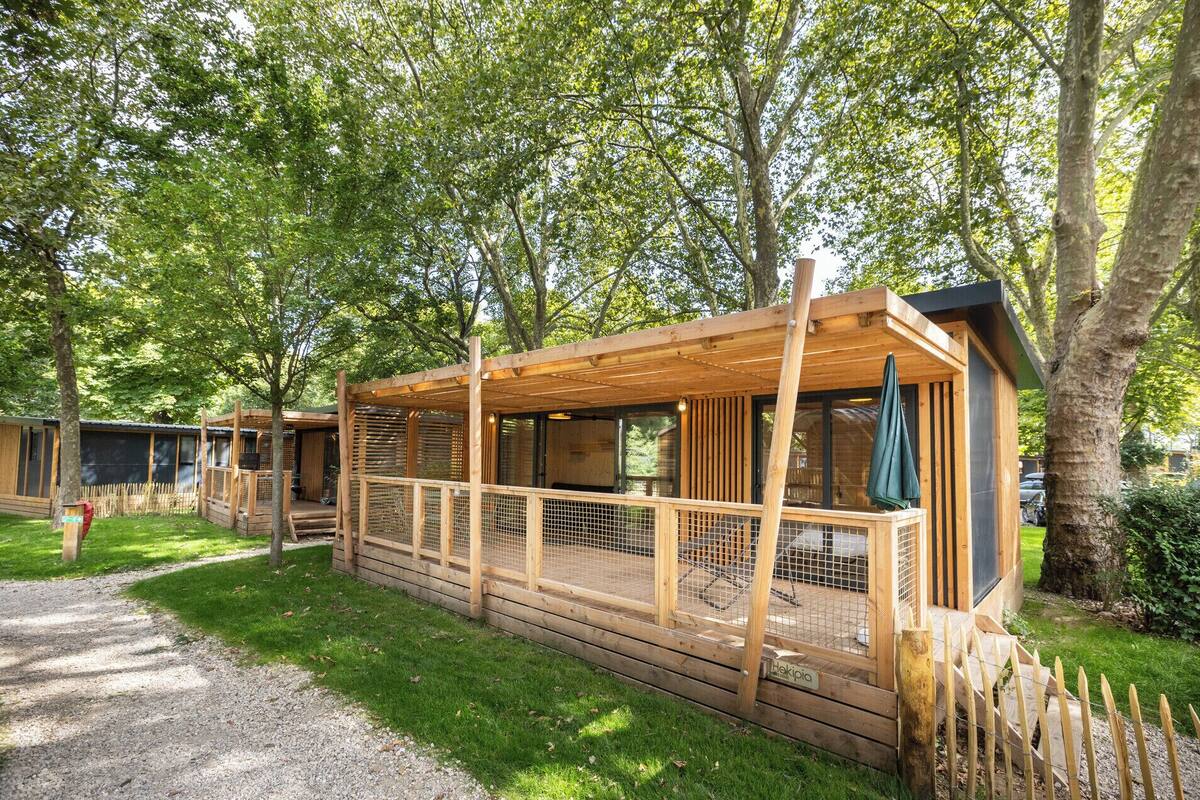Une cabane en bois dotée d’un porche, entourée d’arbres.