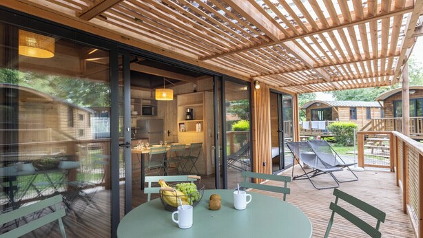 A covered outdoor dining area with a table, chairs, and a view of the surrounding landscape. - Camping de l'Ill Colmar (Horbourg-Wihr)
