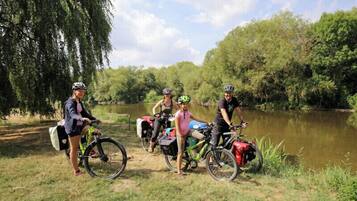 Four cyclists with bicycles near a body of water, surrounded by trees.