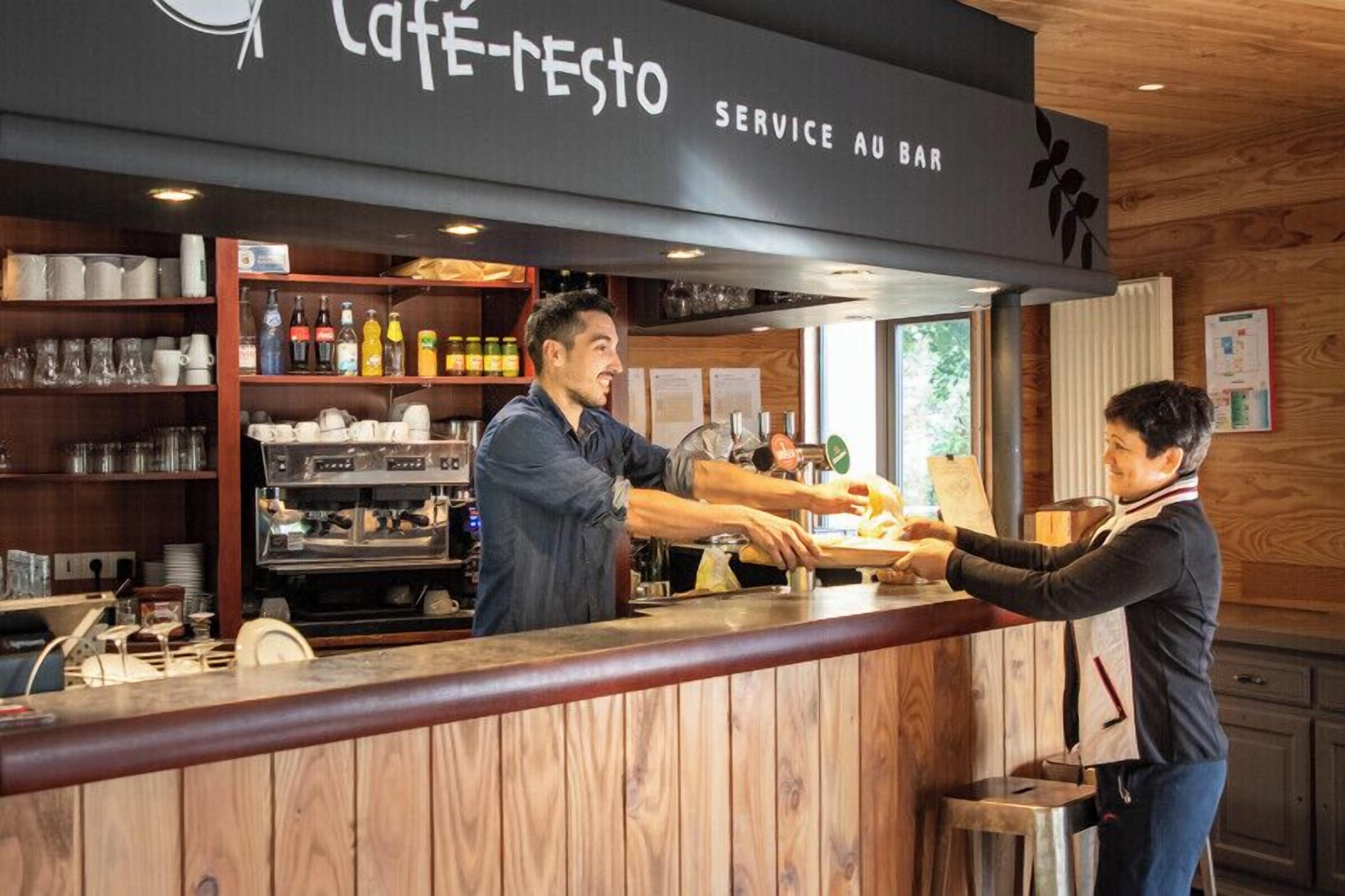 A café-resto with a bar service area, wooden interior, and shelves stocked with various items.