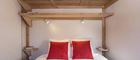 A bed with a wooden headboard, two red pillows, and a brown blanket.