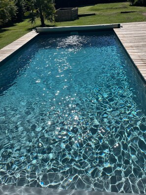 Una piscina rectangular con agua azul cristalina y una cubierta de madera alrededor.