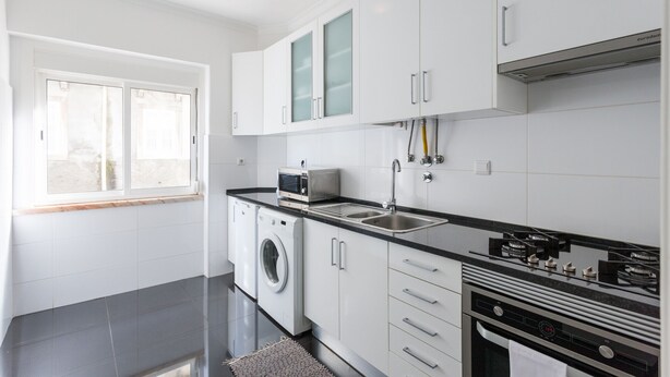 Una cocina moderna con armarios blancos, microondas integrado, lavadora y un lavaplatos de acero inoxidable.