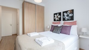 Una cama bien tendida con sábanas blancas, un armario de madera y dos cuadros de flores colgados en la pared.