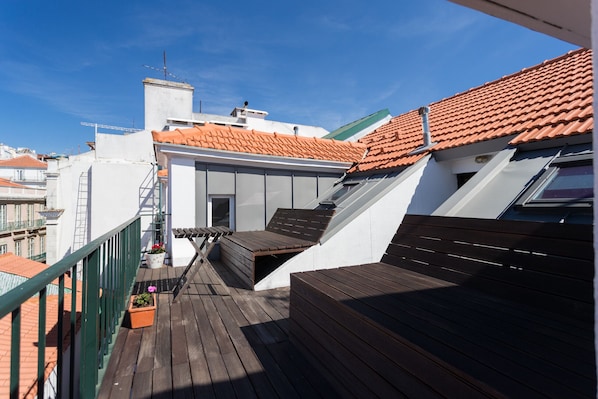 Une terrasse sur le toit, dotée d’un sol en bois, d’un petit espace salon et offrant une vue sur les bâtiments adjacents.