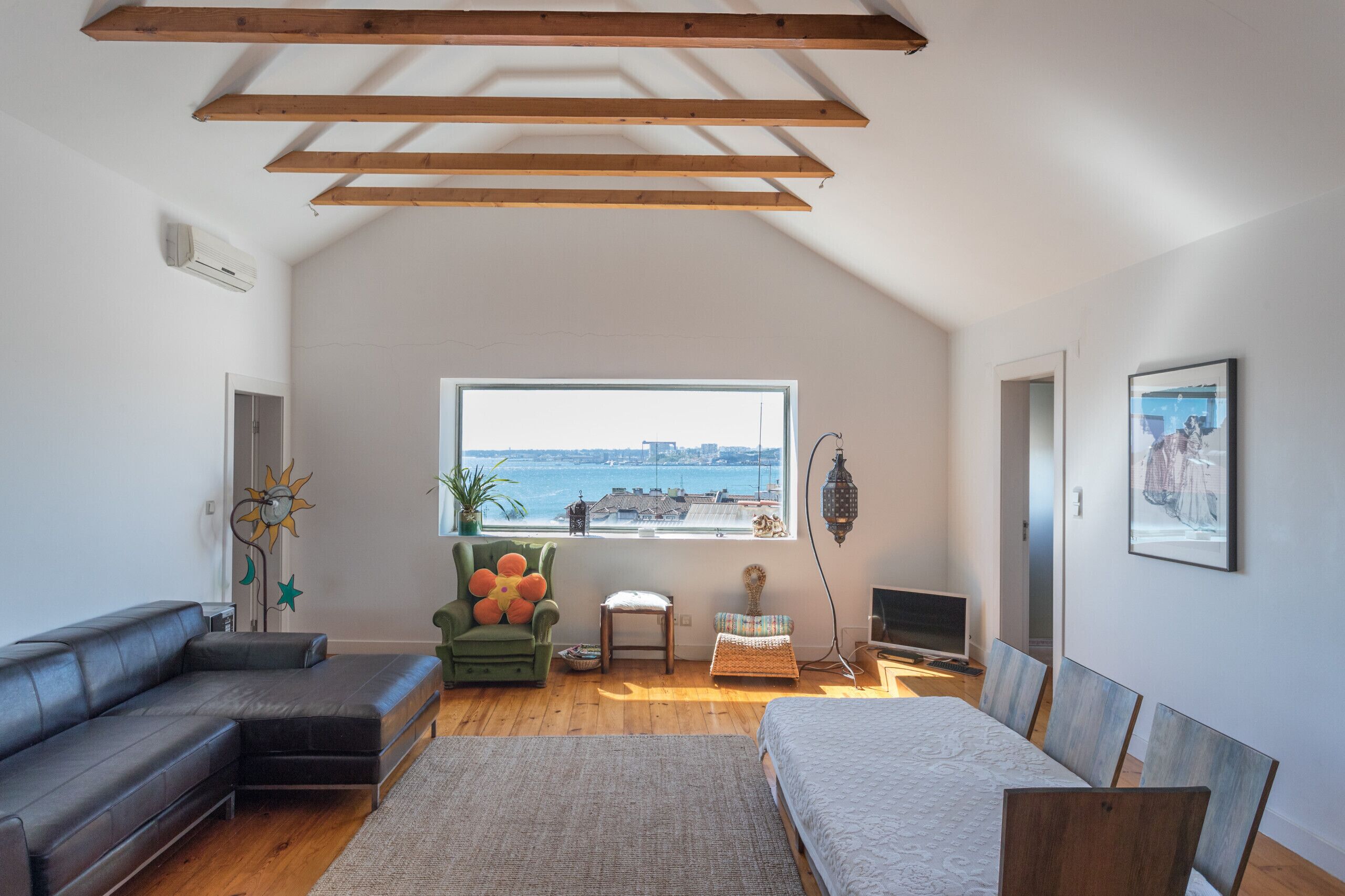 A modern loft bedroom with a large window, a green armchair, a sofa, and a bed.
