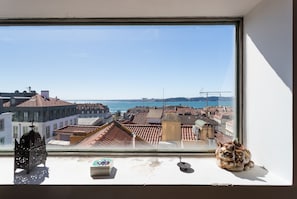 A window with a view of a coastal cityscape, a decorative lantern, and a ceramic cat figurine on the windowsill.