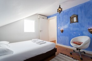 A bedroom with a white bed, a blue accent wall, a white chair, and a small window. - FLH Chiado Skyline (Lisbon)